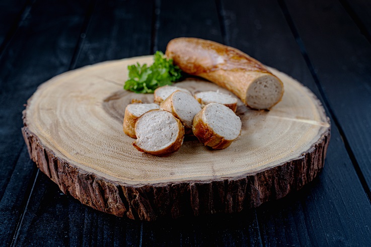 Damhus Bratwurst, gebraten-geschnitten, 3000g Eine gebratene, geschnittene Bratuwurst auf einem Holzbrett.